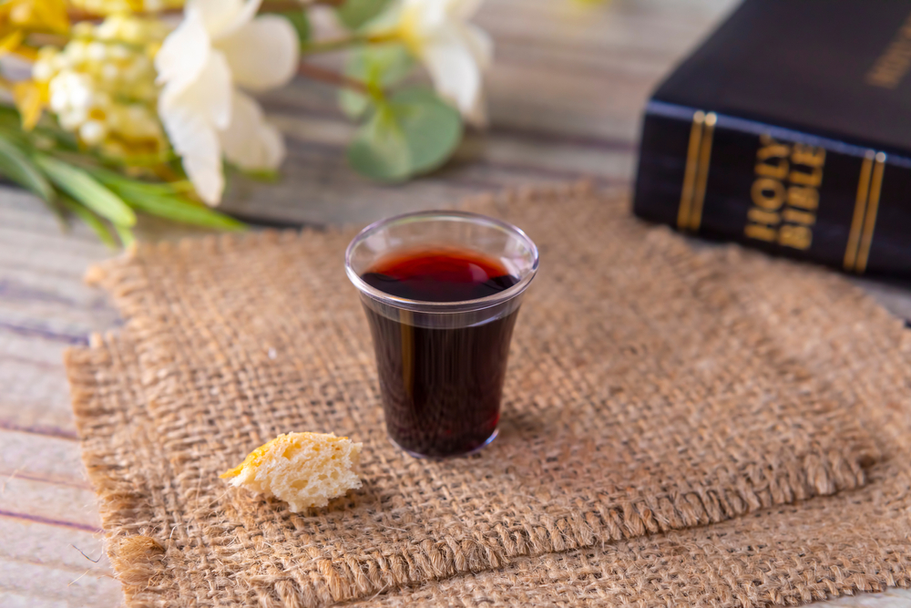 Wine and bread symbolizing Communion with bible and flowers in the background