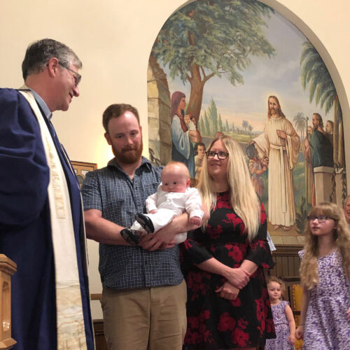 Father holding baby boy with mother and two daughters preparing for Baptism of baby