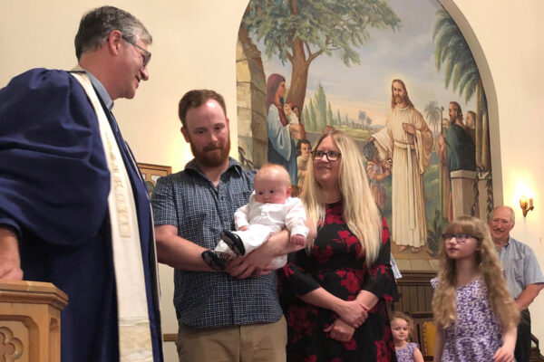 Father holding baby boy with mother and two daughters preparing for Baptism of baby