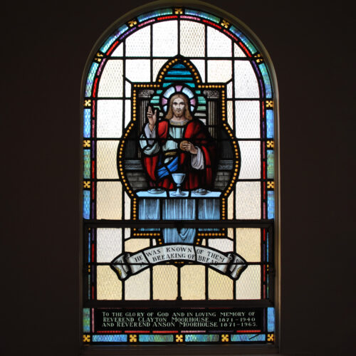 Stained glass window depicting Jesus at a table with chalice holding bread