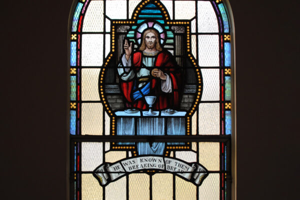 Stained glass window depicting Jesus at a table with chalice holding bread