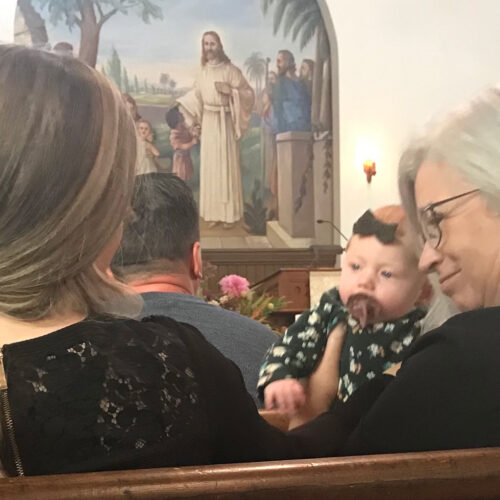 Three generations, grandma holding granddaughter with daughter sitting beside her in pew