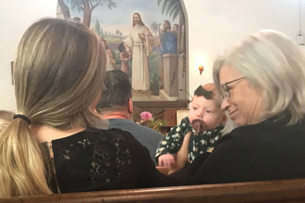 Three generations, grandma holding granddaughter with daughter sitting beside her in pew