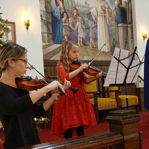 Woman and child playing violins with Christmas tree in the background