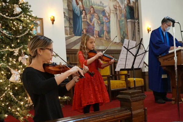 Woman and child playing violins with Christmas tree in the background