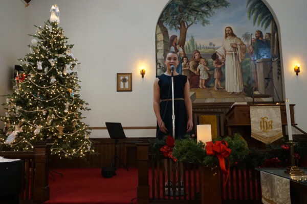 Girl singing into microphone with a Christmas tree in the background